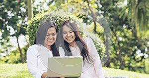 Asian two women talking using laptop sitting on green meadow at park. Friendship girls chat and talk look at laptop planning do