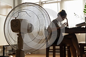 Asian unhappy woman sitting in front of working fan suffering