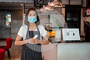 Asian waitress woman wearing face masks and holding an infrared forehead thermometer to check body temperature for virus symptoms