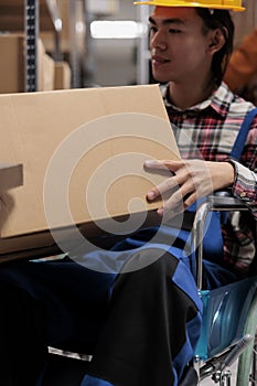 Asian warehouse order picker wheelchair user holding customer parcel