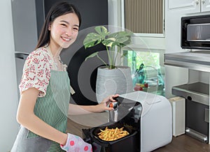 Asian wife cooking fries chicken by use her electric fryer in her kitchen at home