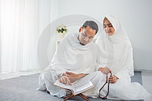 Asian wife and husband praying with Al-Qur`an and tasbih