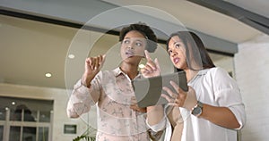 Asian woman and African American woman discuss a project on a tablet in a business office setting