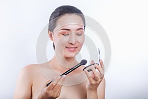 Asian woman applying cosmetic powder brush on white background