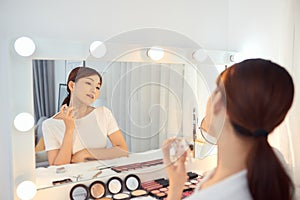 Asian Woman applying fragrance with a spray in front of a make up mirror