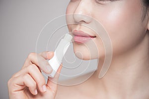 Asian woman applying hygienic lip balm over grey background