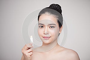 Asian woman applying hygienic lip balm over grey background