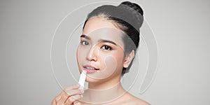 Asian woman applying hygienic lip balm over grey background