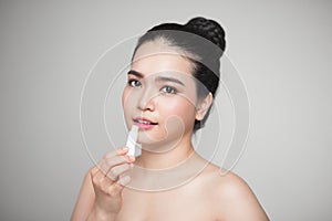 Asian woman applying hygienic lip balm over grey background