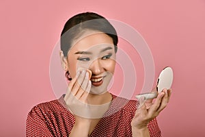 Asian woman applying makeup cosmetics while looking at the mirror, Midday face powder foundation touch up to keep looking fresh.