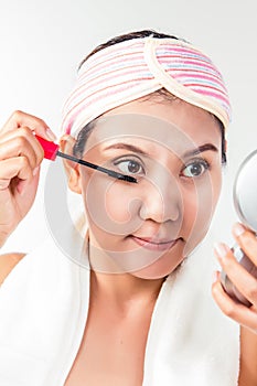 Asian woman applying mascara makeup on eyes by brush