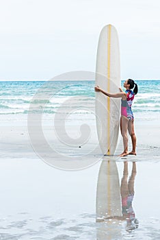 Asian woman attractive and young standing on the beach, holding a white surfboard
