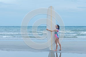 an Asian woman attractive and young standing on the beach, holding a white surfboard