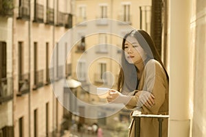 Asian woman in balcony thinking - outdoors lifestyle portrait of young beautiful and thoughtful Japanese girl at drinking morning