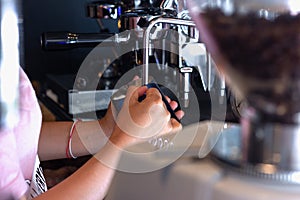 Asian woman Barista holding pitcher and controls temperature for preparing milk foam for cappuccino or latte coffee