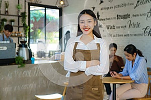 Asian woman Barista or owner small business in apron looking at camera ready to give Coffee Service with customer in background at