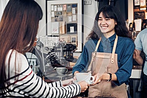 Asian woman barista wear jean apron holding coffee cup served to