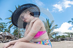 An asian woman at the beach experiences dull shoulder pain, nerve impingement or soreness while on vacation