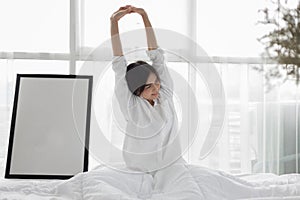 Asian woman Beautiful young smiling woman sitting on bed and stretching in the morning at bedroom after waking up in her bed full