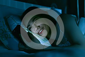 Asian woman on bed late at night texting using mobile phone tire