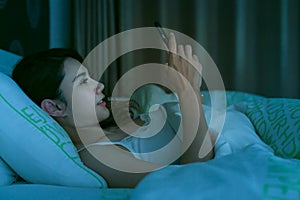 Asian woman on bed late at night texting using mobile phone tire