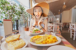 Asian woman in big hat having meal with greek salad Horiatiki in restaurant. Greece cuisine concept