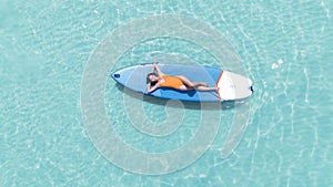 Asian woman in bikini sleep and relax on paddle board on the beach