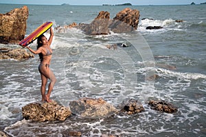 An Asian woman in a bikini is standing carrying a surf board on the beach.