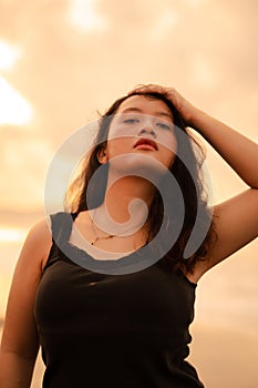 an Asian woman in a black dress and plump body strikes a very coquettish pose while enjoying the beach