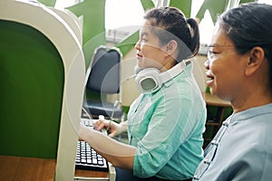 Asian woman with blindness disability using computer keyboard and braille display assistive device working with senior colleague