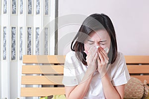 Asian woman blowing her nose while sitting on bed. illness woman