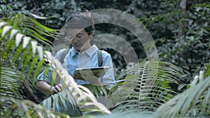Asian woman botanist is researching plant species and working on digital tablet in tropical rainforest. Biology activist.