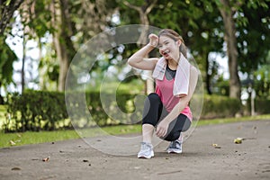 An Asian Woman Is break from jogging With A Gentle Smile In The Park Is Full Of Trees. Looks Around The Park and Smiles While