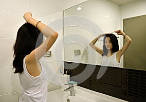 Asian woman brushing hair in front of mirror in bathroom