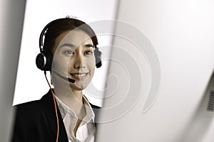 Asian woman call centre working use headset look at computer screen. Portrait of smiling Asian female customer service