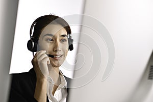 Asian woman call centre working use headset look at computer screen. Portrait of smiling Asian female customer service agent