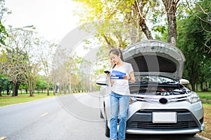 Asian woman calling for assistance with his car broken down by the roadside. She called the mechanic and waited by the car for