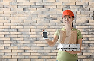 Asian woman with cardboard pizza boxes, paper bag and mobile phone on brick wall background. Food delivery service