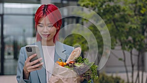 Asian woman carrying grocery bag and using smartphone