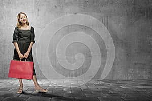 Asian woman carrying a shopping bag with a black wall background