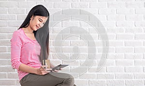 Asian woman in casual cloth holding credit card and using to online shopping with tablet at white brick wall.Digital technology l