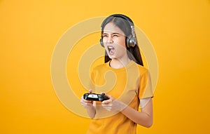 Asian woman in casual yellow t-shirt and playing video games using joysticks with headphones on orange background.