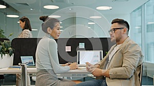 Asian woman and Caucasian man coworkers talking in open space office at desk