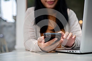 An Asian woman checking messages on her smartphone while working on her laptop at a cafe