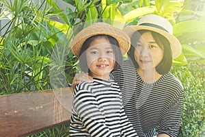 Asian woman and child sitting relax together on wooden bench, They smiling and feeling happiness.