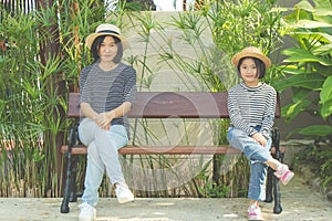 Asian woman and child sitting relax together on wooden bench, They smiling and feeling happiness.