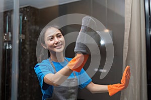 Asian woman cleaning the glass in the apartment. Cleaning staff maintain cleanliness in with towel and spray detergent