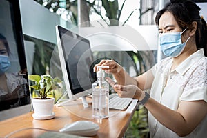 Asian woman cleaning hands with hand sanitizer after use and before starting work on computer at office,avoid contaminating with