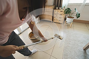 Asian woman cleaning and mopping the floor with a microfiber wet mop pad in the living room. Woman doing chores at home.