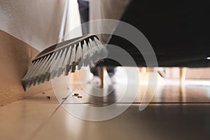 Asian woman cleaning and sweeping dust the floor under the sofa with a broom in the living room.